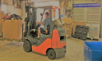 Man on forklift moves credential clothing in warehouse