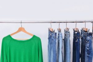 A green sweater hung up next to jeans on a rack