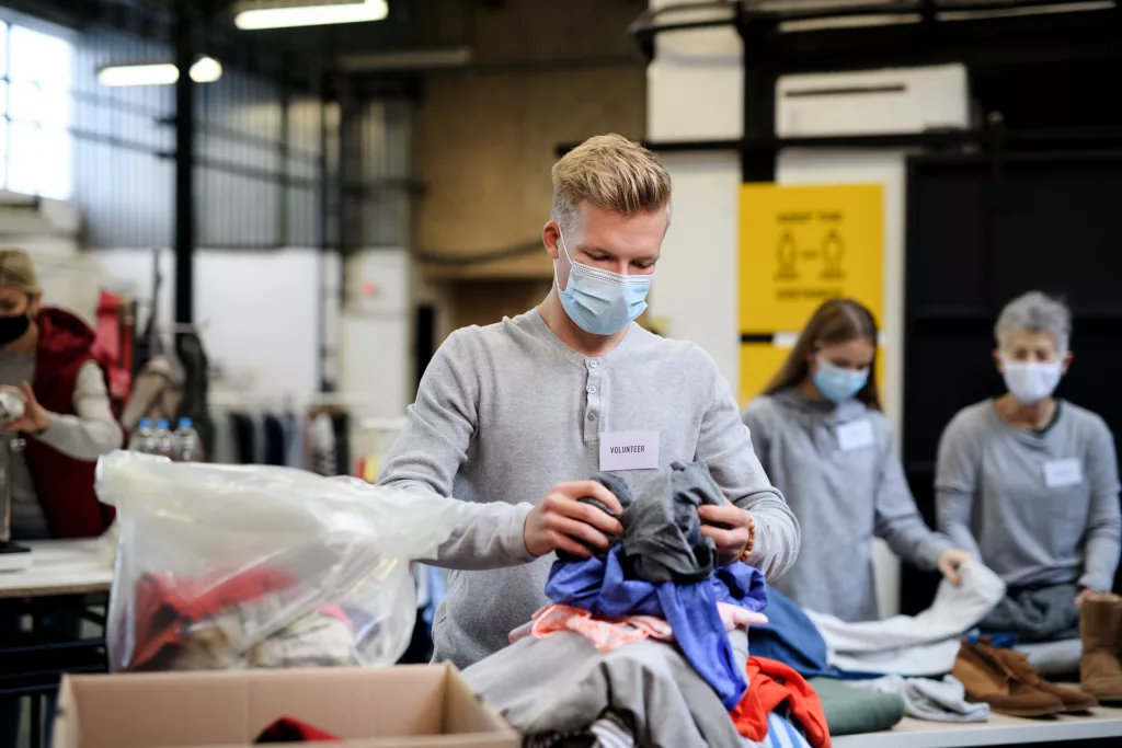 Portrait of volunteers sorting out donated clothes in community charity donation center, coronavirus concept.