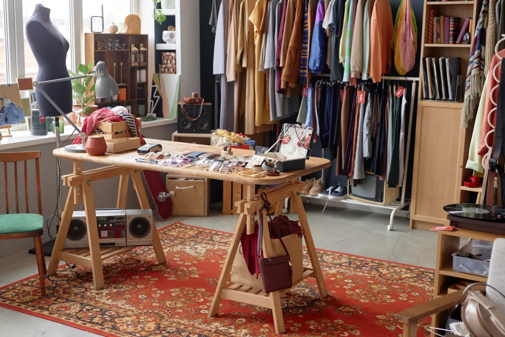 Interior of thrift store or second hand shop selling pre owned clothing hanging on rack and fashion accessories displayed on table