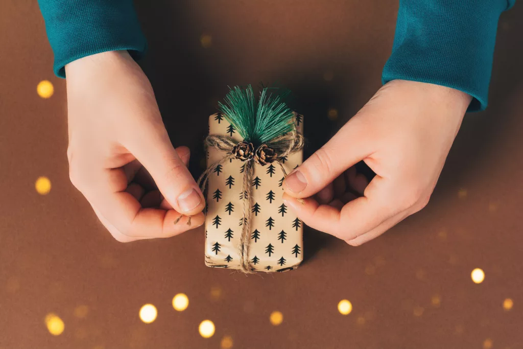 Male hands are packing a gift box on the eve of holidays Christmas and New Year on brown background. Eco-friendly concept, zero waste christmas.