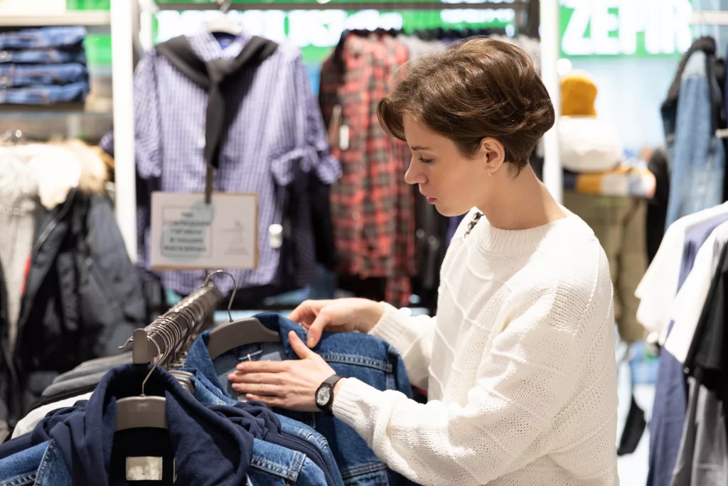 young woman chooses clothes in second hand.